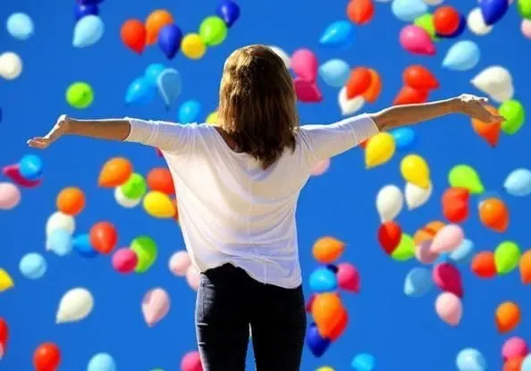 Personne les bras ouverts sous un ciel rempli de ballons, pour illustrer la confiance en soi
